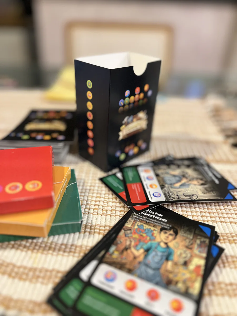 O protótipo de papel da Loomty sobre a mesa de casa: cartas ilustradas espalhadas ao lado da caixa e dos baralhos coloridos